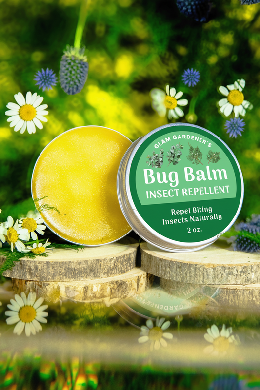 A photo of Glam Gardener NYC’s Bug Balm Natural Bug Repellent featuring a floral background. The product is in a 2 ounce aluminum tin that features a screw cap. It is all natural and crafted with beeswax, olive oil, and essential oils including citronella, eucalyptus, cedarwood, and lemongrass. This is showcasing the front label.