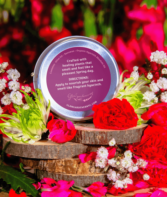 Hyacinth Blooms Scented Salve is Glam Gardener's Signature salve infused with authentic Hyacinth Absolute Oil. The label is a dual toned pink color and the backrgound showcases flowers. The salve contains a creamy solid perfume and hydrating lotion made with Olive Oil, absolute oil, and beeswax. The back label reads "Crafted with healing plants that smell and feel like a pleasant Spring day. Apply to nourish your skin and smell like fragrant hyacinth"