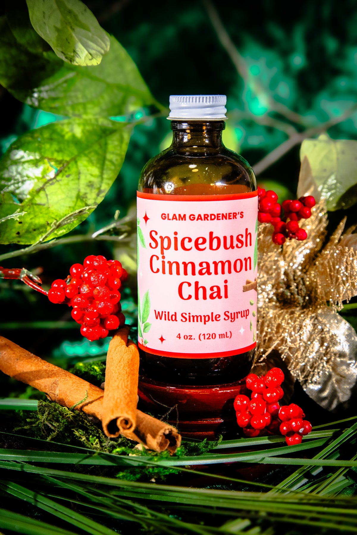 Glam Gardener's Spicebush Cinnamon Chai Simple Syrup with organic and wildcrafted ingredients. Cinnamon, Wild Spicebush (Lindera benzoin), Cardamom. Organic sugar and handcrafted. Red label and floral background. Hand harvested wild spicebush leaves. Simple syrup for fall and winter.