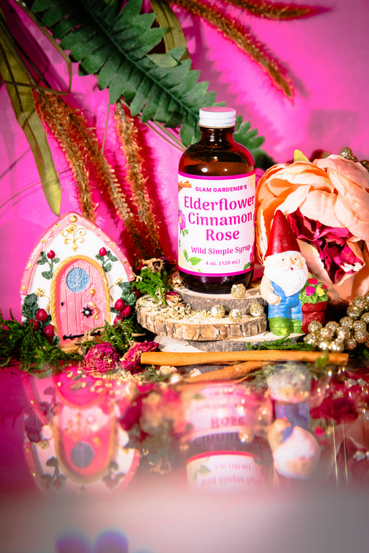 Glam Gardener’s Wildflower Simple Syrup with Elderflower, Cinnamon, and Rose. Handcrafted four ounce bottle on pink background with floral and whimsy elements.