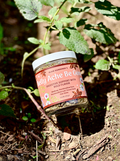 A jar of belly ache relief herb blend by Glam Gardener's is shown outdoors nestled among native Skullcap and soil.