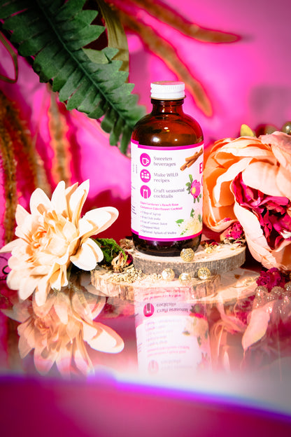 Glam Gardener’s Wildflower Simple Syrup with Elderflower, Cinnamon, and Rose. Handcrafted four ounce bottle on pink background with floral and whimsy elements.