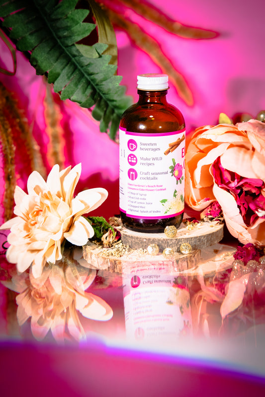 Glam Gardener’s Wildflower Simple Syrup with Elderflower, Cinnamon, and Rose. Handcrafted four ounce bottle on pink background with floral and whimsy elements.