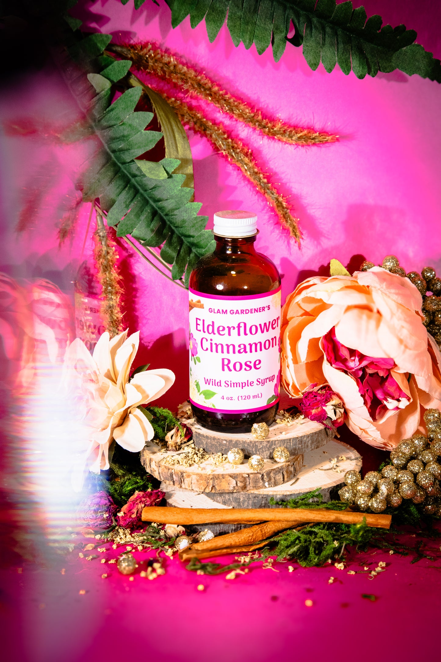 Glam Gardener’s Wildflower Simple Syrup with Elderflower, Cinnamon, and Rose. Handcrafted four ounce bottle on pink background with floral and whimsy elements.