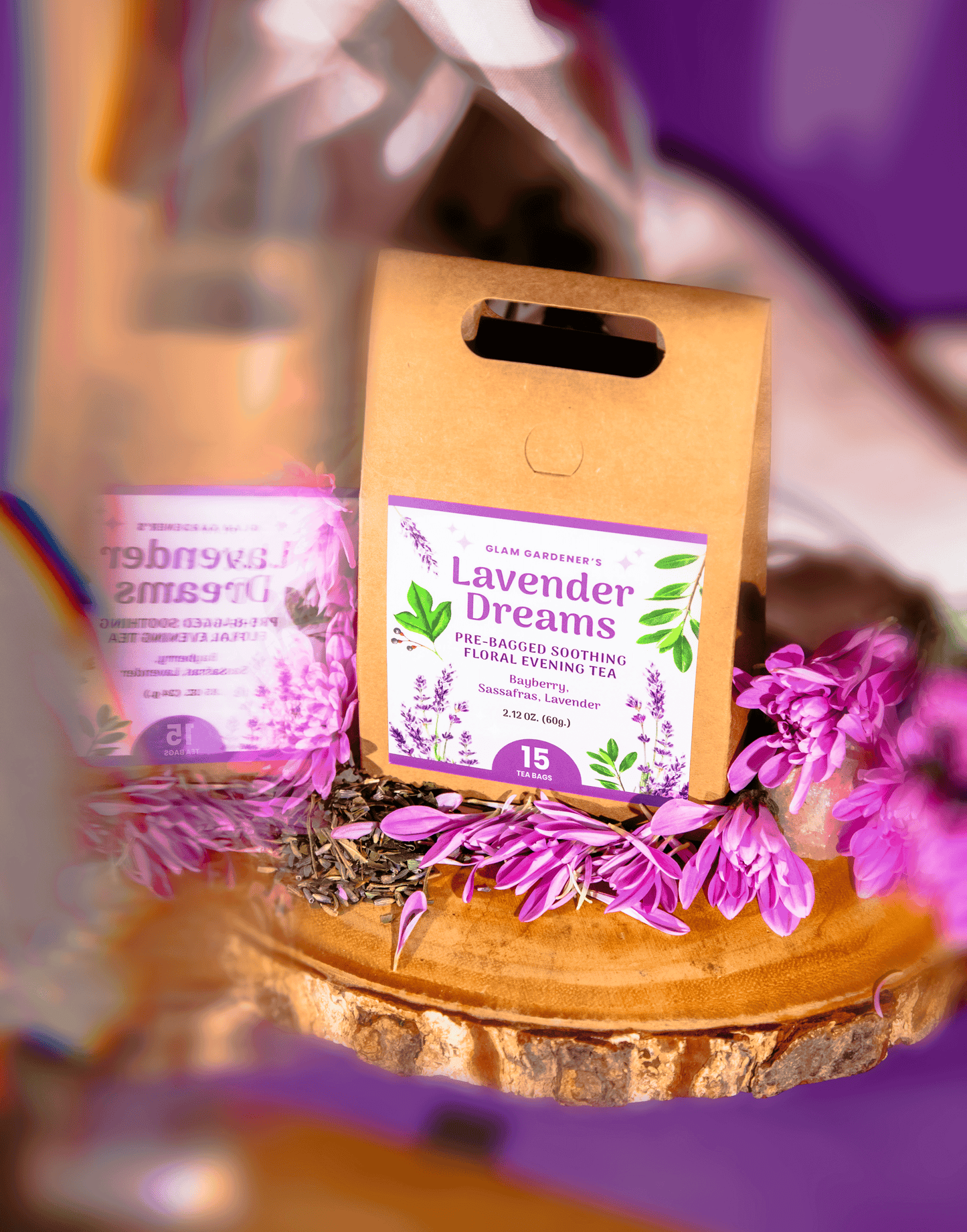 A kraft paper stand bag labeled 'Lavender Dreams' surrounded by purple flowers on a reflective surface with a purple and warm-toned blurred background. By Glam Gardener with Bayberry Sassafras, and Lavender