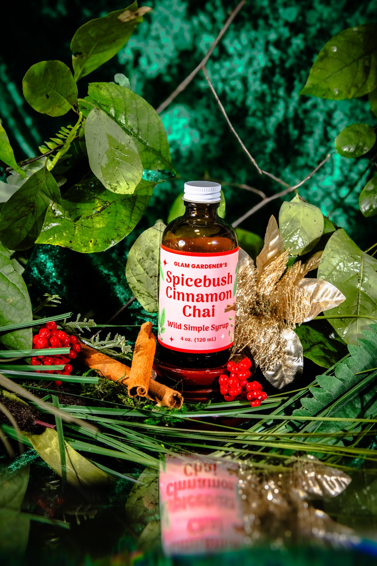 Glam Gardener's Spicebush Cinnamon Chai Simple Syrup with organic and wildcrafted ingredients. Cinnamon, Wild Spicebush (Lindera benzoin), Cardamom. Organic sugar and handcrafted. Red label and floral background. Hand harvested wild spicebush leaves. Simple syrup for fall and winter.