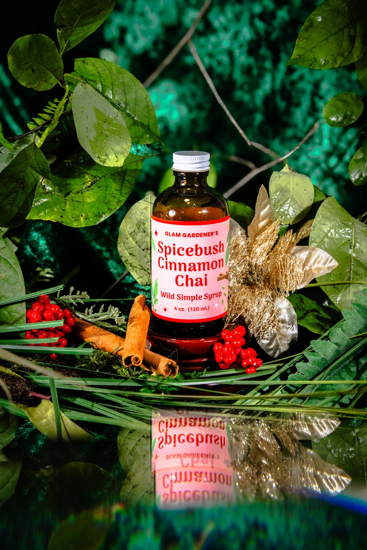 Glam Gardener's Spicebush Cinnamon Chai Simple Syrup with organic and wildcrafted ingredients. Cinnamon, Wild Spicebush (Lindera benzoin), Cardamom. Organic sugar and handcrafted. Red label and floral background. Hand harvested wild spicebush leaves. Simple syrup for fall and winter.