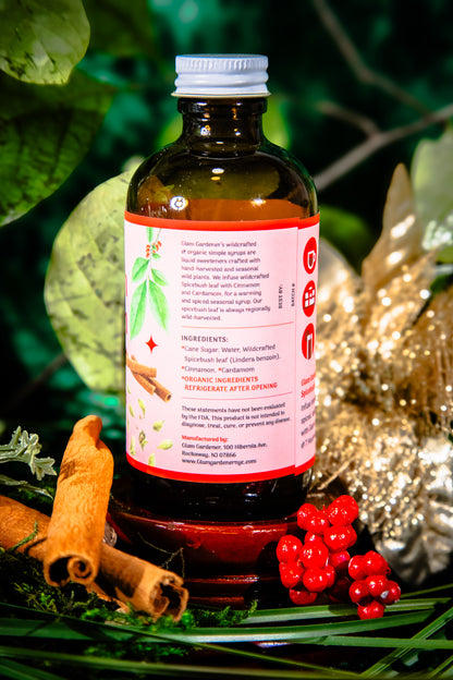 Glam Gardener's Spicebush Cinnamon Chai Simple Syrup with organic and wildcrafted ingredients. Cinnamon, Wild Spicebush (Lindera benzoin), Cardamom. Organic sugar and handcrafted. Red label and floral background. Hand harvested wild spicebush leaves. Simple syrup for fall and winter.