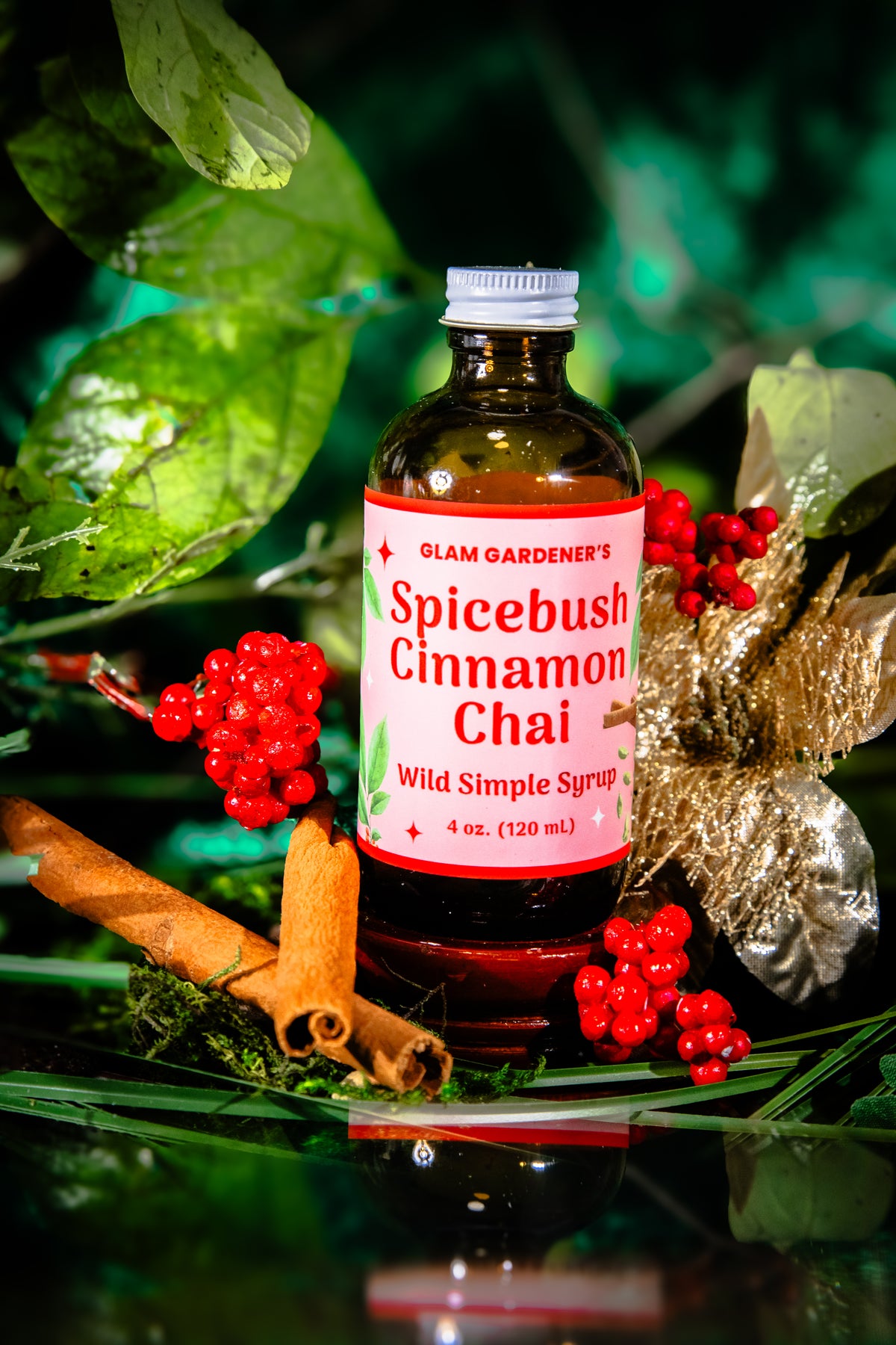 Glam Gardener's Spicebush Cinnamon Chai Simple Syrup with organic and wildcrafted ingredients. Cinnamon, Wild Spicebush (Lindera benzoin), Cardamom. Organic sugar and handcrafted. Red label and floral background. Hand harvested wild spicebush leaves. Simple syrup for fall and winter.