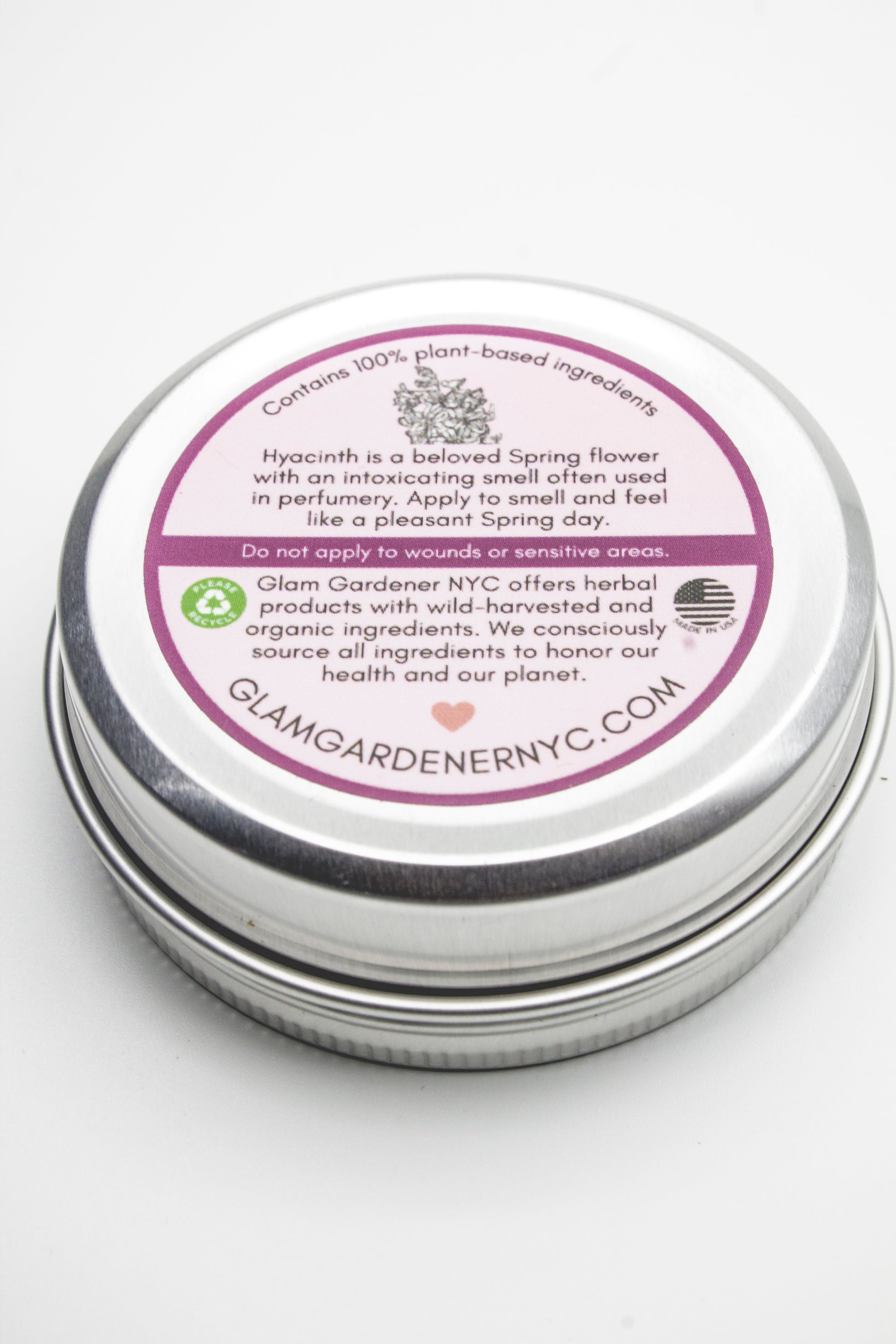 Metallic tin with a purple label on a white background with the following text: Contains 100% plant-based ingredients. Hyacinth is a beloved Spring flower with an intoxicating smell often used in perfumery. Apply to smell and feel like a pleasant Spring day. Do not apply to wounds or sensitive areas. Glam Gardener NYC offers herbal products with wild-harvested and organic ingredients. We consciously source all ingredients to honor our health and our planet. Glamgardenenryc.com